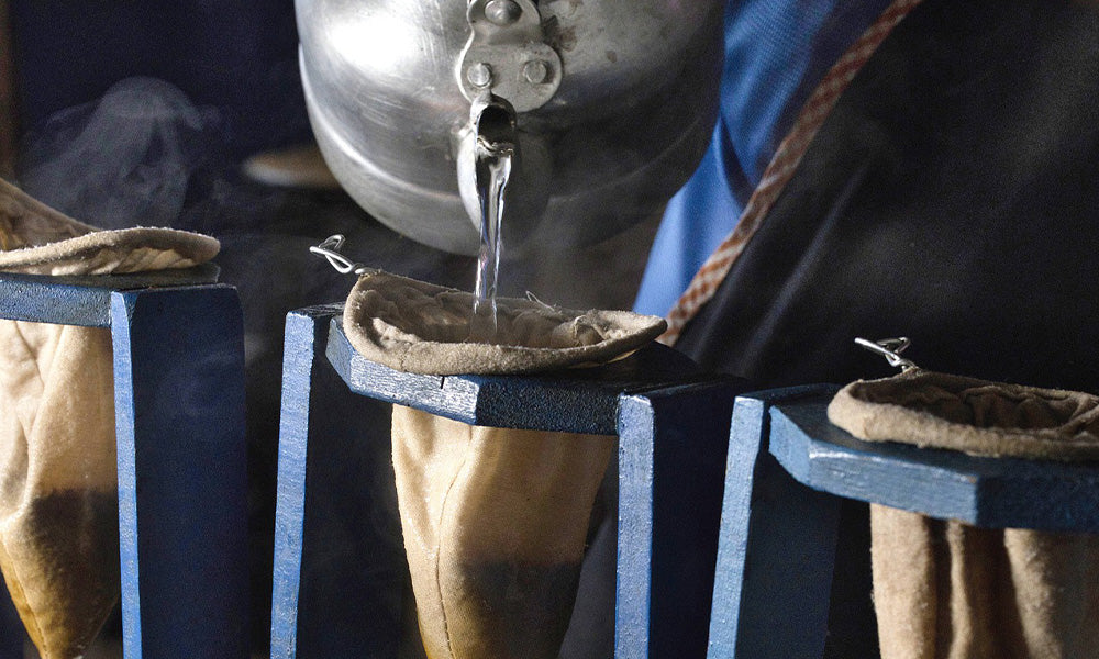 ouring hot water in a circular motion over coffee grounds in the cotton bolsita of a wooden Costa Rica chorreador